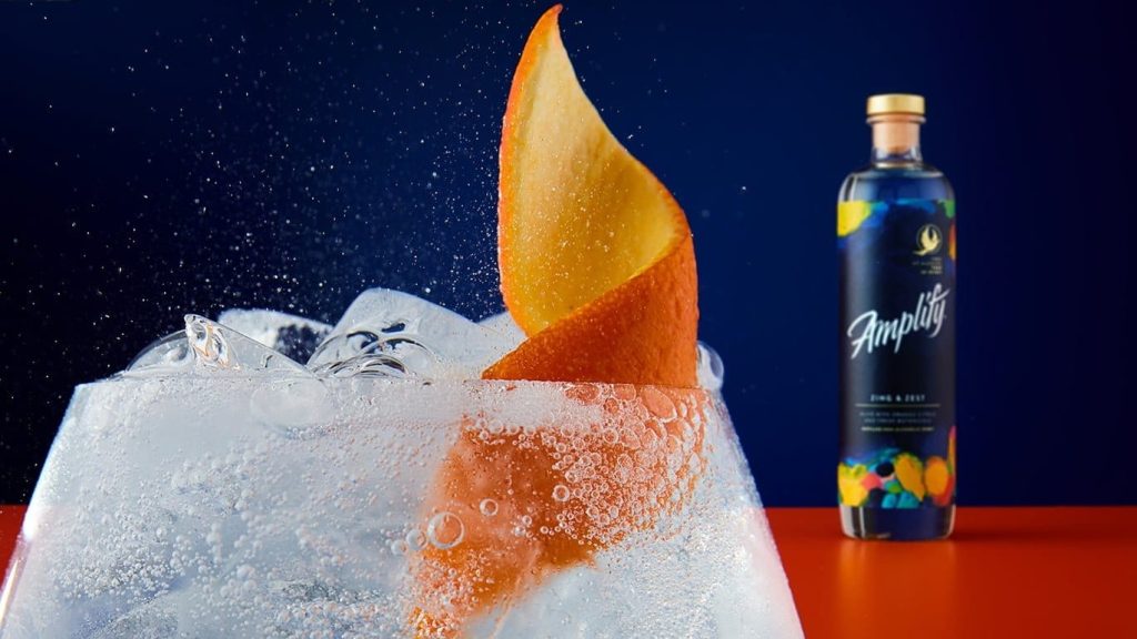 cocktail with an orange peel and a bottle of amplify alcohol free spirit in the background